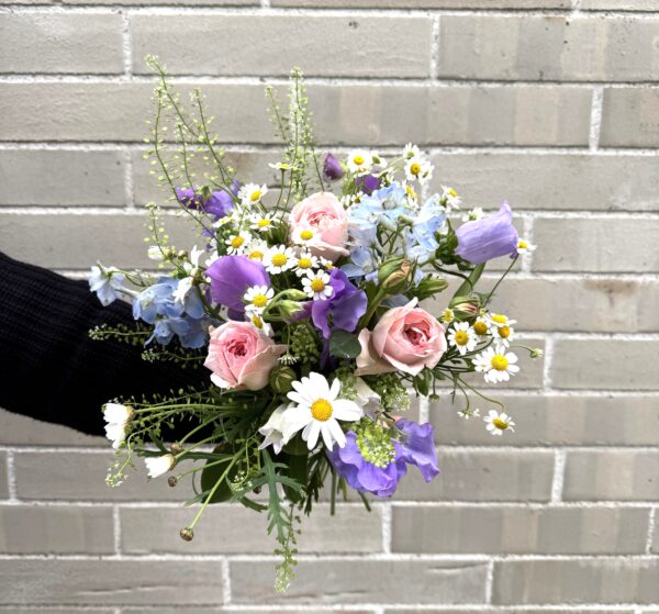 Ein tänzelnder Strauß aus zarten Frühsommerblumen wie Margeriten, Kamille, Glockenblume, Wicke und Rittersporn kommt doch überall gut an. Die feinen Blumen verleihen dem Strauß seine aufgelockerte Wirkung und die pastellenen Farben bringen die Leichtigkeit. Von klein und fein bis mittelgroß – dieser, eher kurz gebundene Strauß, eignet sich besonders gut für den Esstisch und bringt zugleich einen leichten Duft mit. „Frühsommergefühle“ – noch nicht ganz Sommer, aber bald!